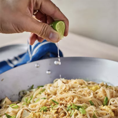 Photo of a hand squeezing a lime into a pasta dish.