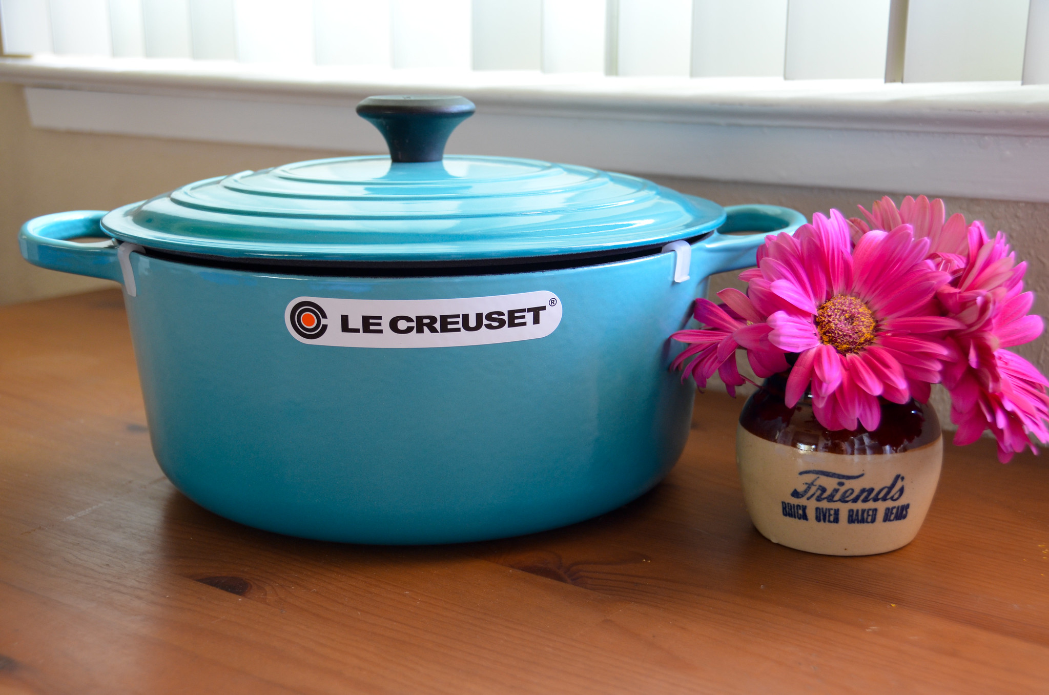 A photograph of a blue Le Creuset oven next to pink flowers.