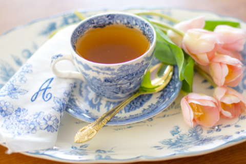 Cup of tea on tea saucer with pink tulips on plate. 