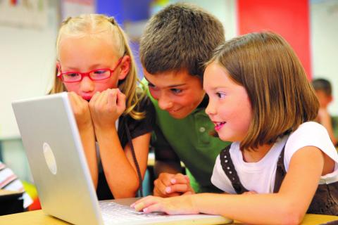 Three children smile and look at a Macbook laptop