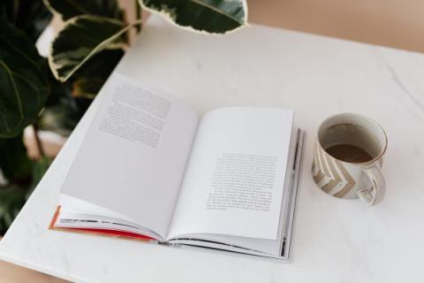 an open book and a cup of coffee or some type of beverage in a coffee cup on a table that is white.