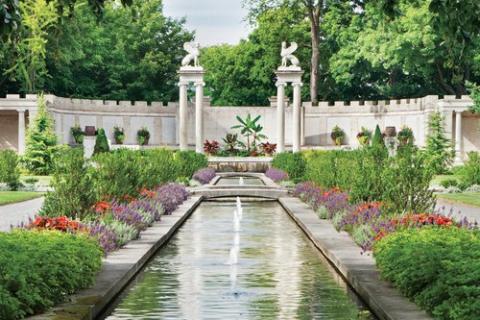 a long fontain surrounded by formal garden and portico in back