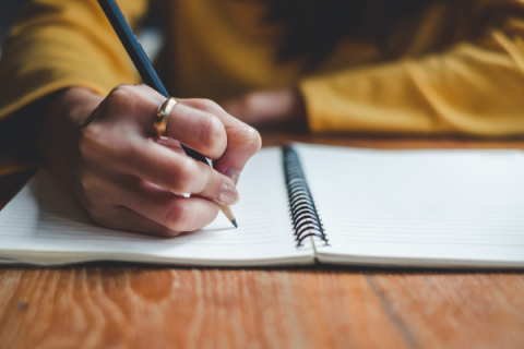 Hand holding pencil writing in notebook