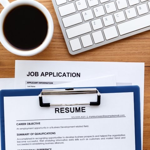 Clipboard with resume attached, coffee cup, and computer keyboard