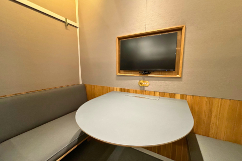 A photograph of the inside of a 4 person study pod, showing a bench, table, and screen.