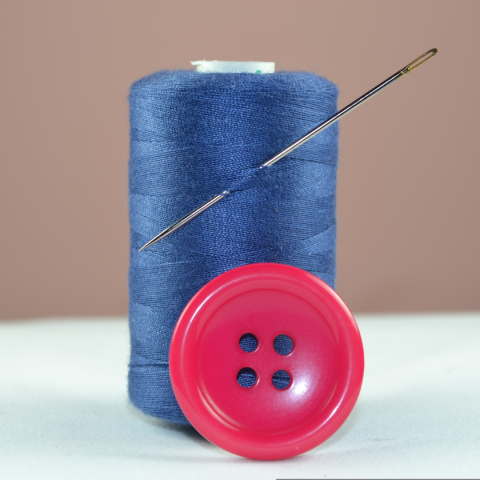 Blue thread with sewing needle stuck through it and pink button. 