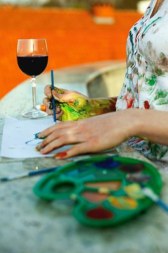 A picture of a woman painting watercolors with a wine glass in the background