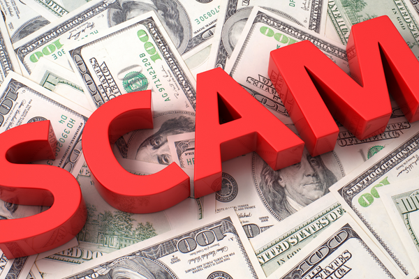 The word scam in bold red over a pile of one hundred dollar bills